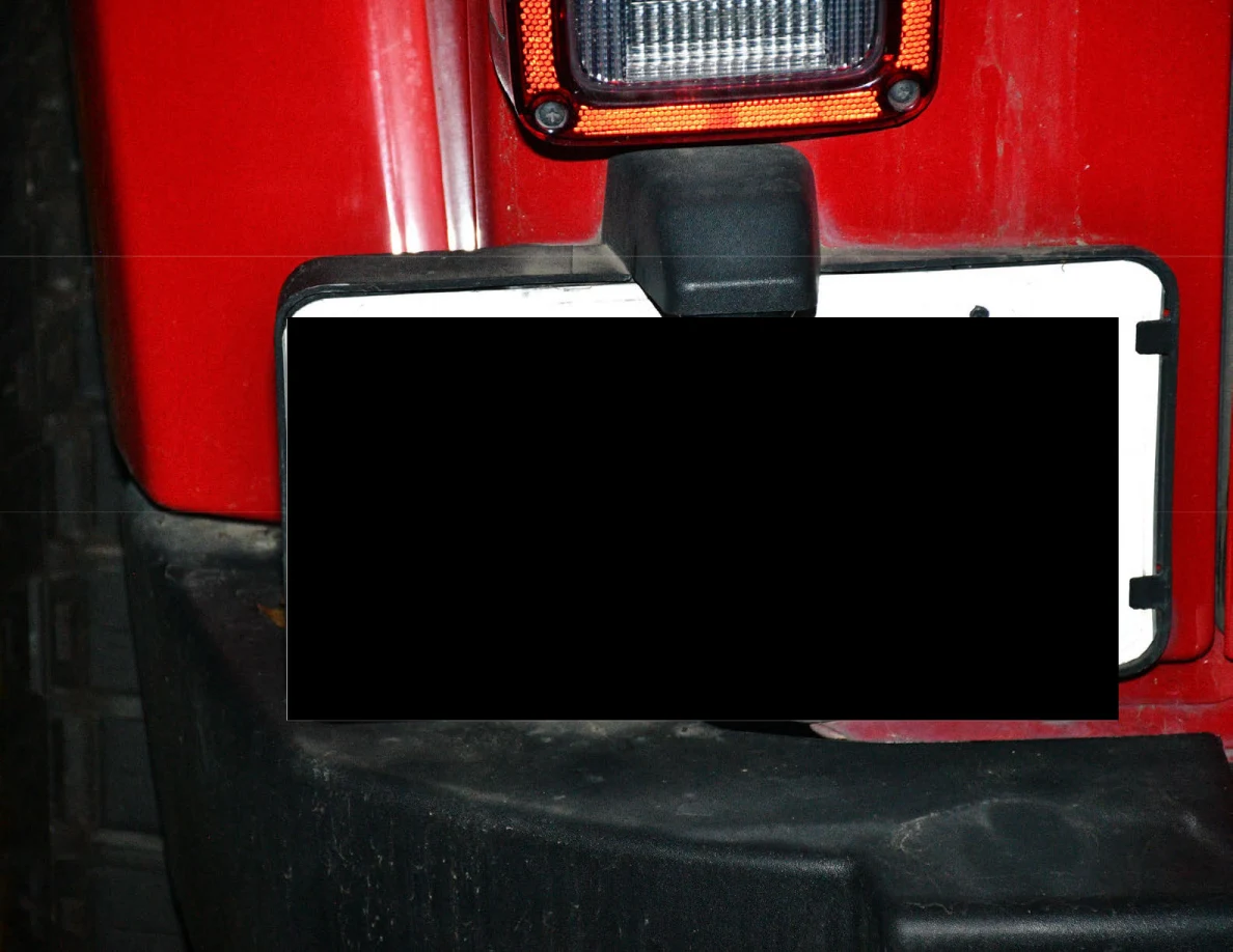 Close view of a red vehicle tail light and redacted license plate.