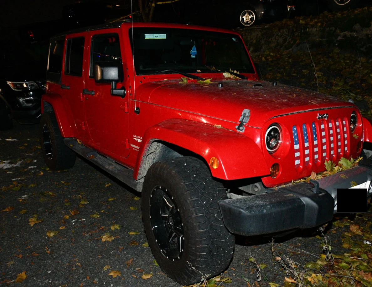 Front and side of a red Jeep parked on fallen leaves.
