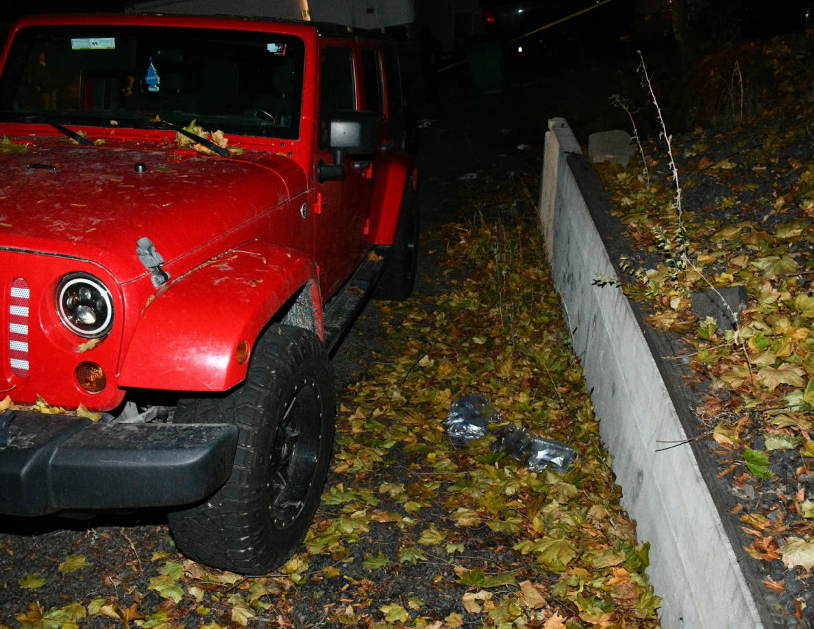 Front of a red Jeep beside a low wall and fallen leaves.