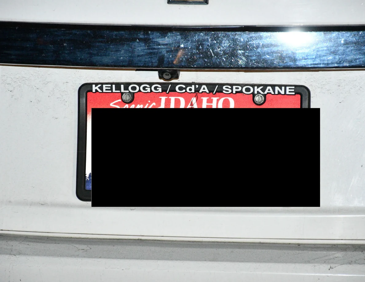 Close view of a redacted Idaho license plate and plate frame on a white car.