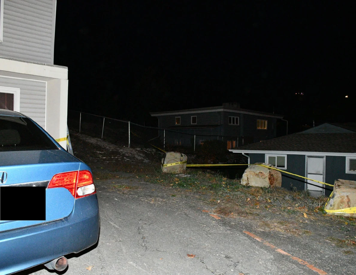 Blue car at the edge of a driveway with boulders and yellow barrier tape.