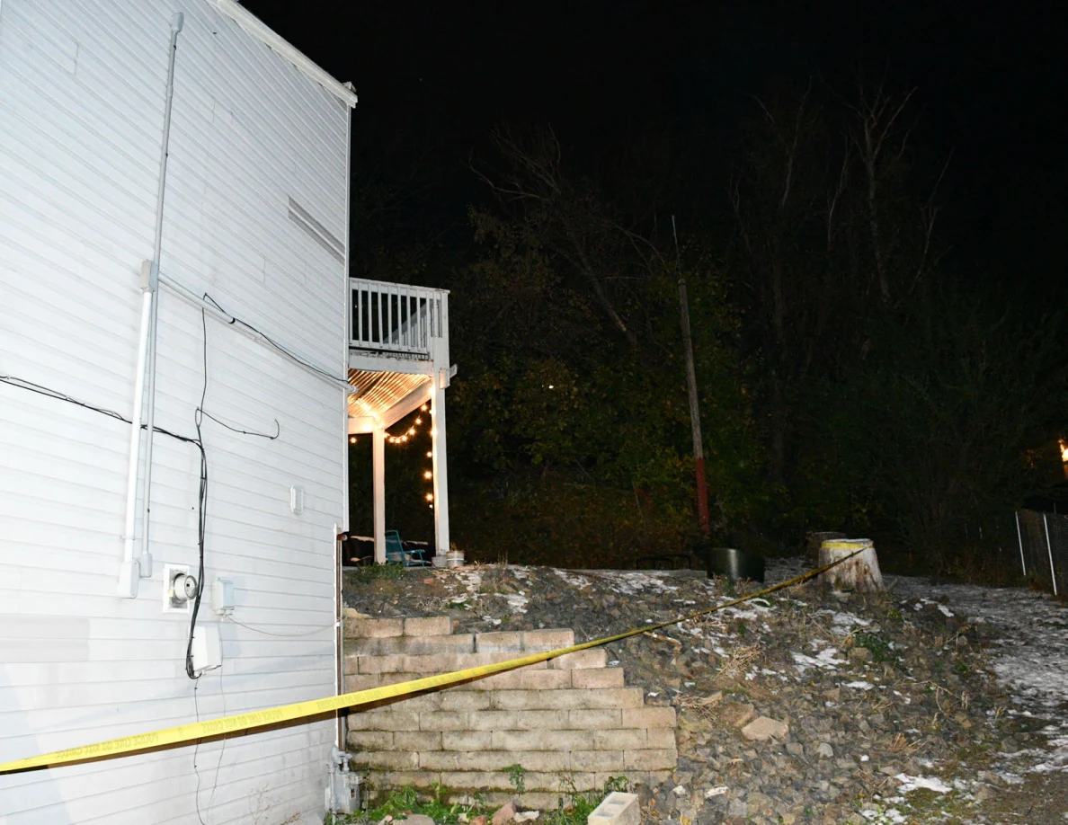 House side wall and utility meter beside a retaining wall and snowy slope.