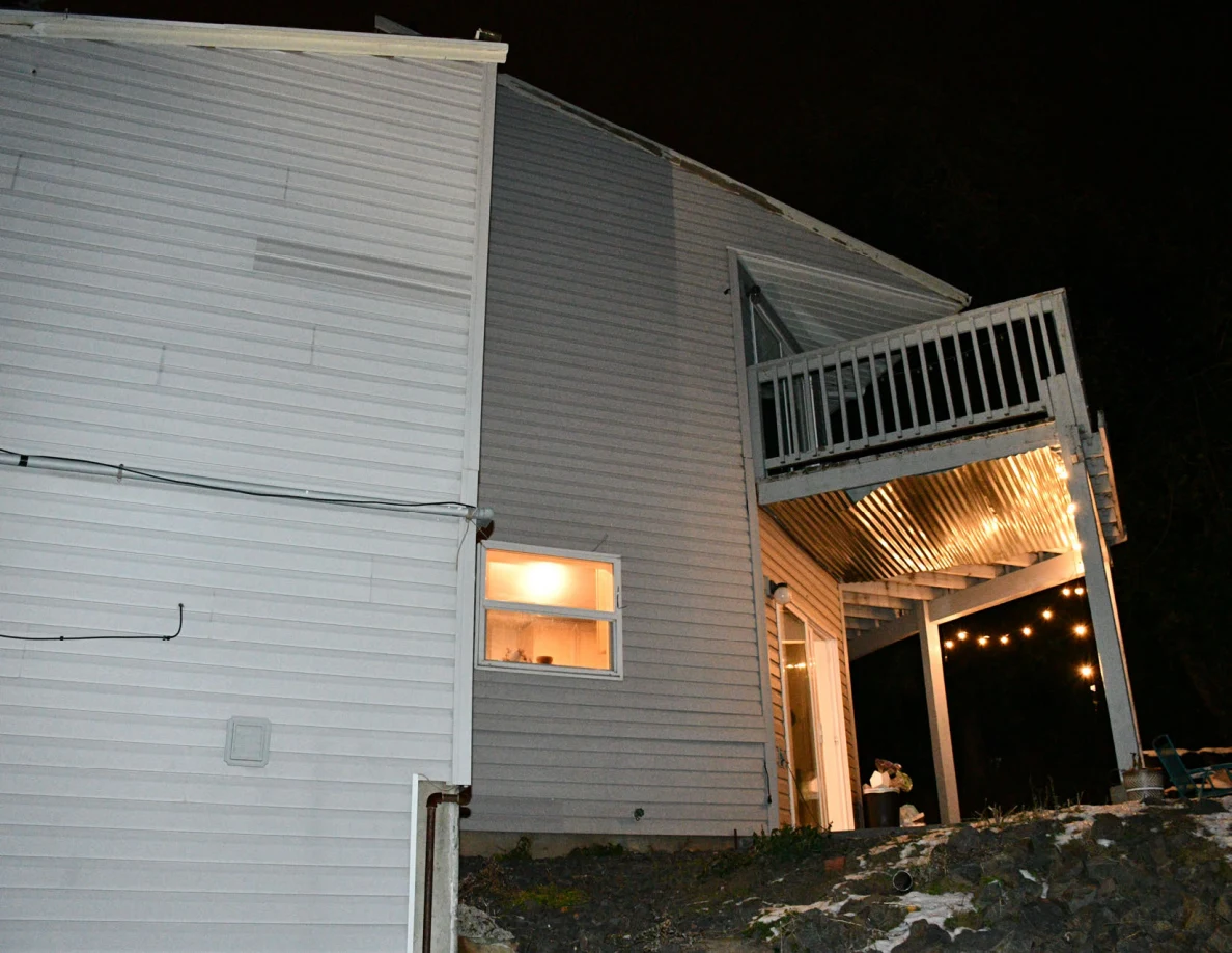 Rear and side house exterior with an upper balcony and illuminated windows.