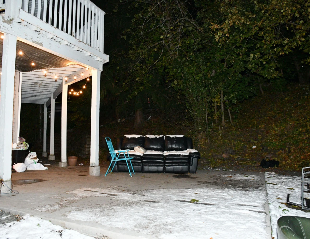 Patio sofa and folding chair beside snow and trees.