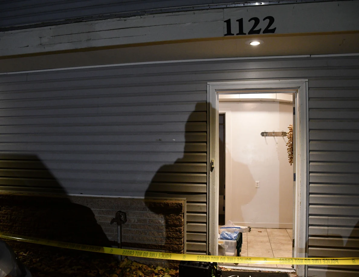 Open front doorway below the number 1122 with yellow barrier tape across the foreground.