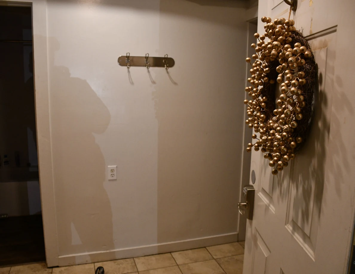 Entryway wall hooks and an open door with a gold-colored wreath.