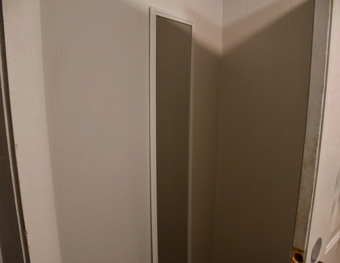 Tall narrow wall mirror beside a doorway.