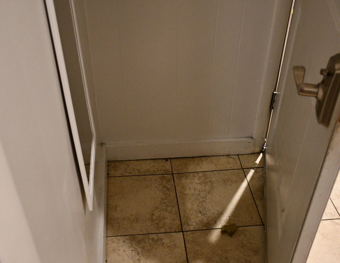Tile floor and lower wall beside an open door and mirror.