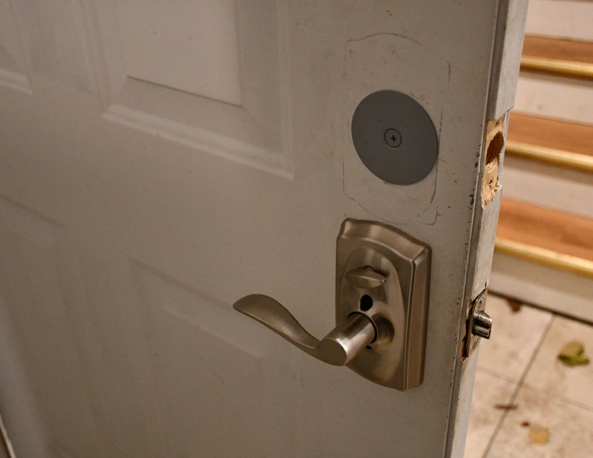 Interior side of a door lock and lever handle with wooden stairs behind.