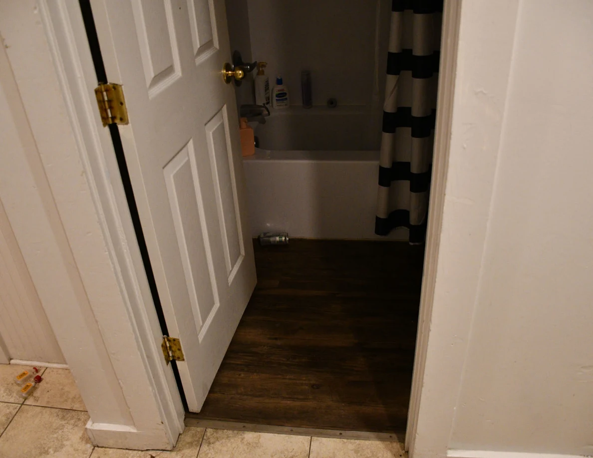 Bathroom doorway with bathtub, toiletries and striped shower curtain.
