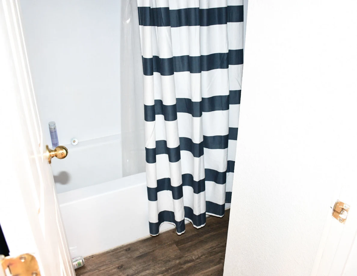 Bathroom doorway showing bathtub, striped shower curtain and wood-pattern floor.