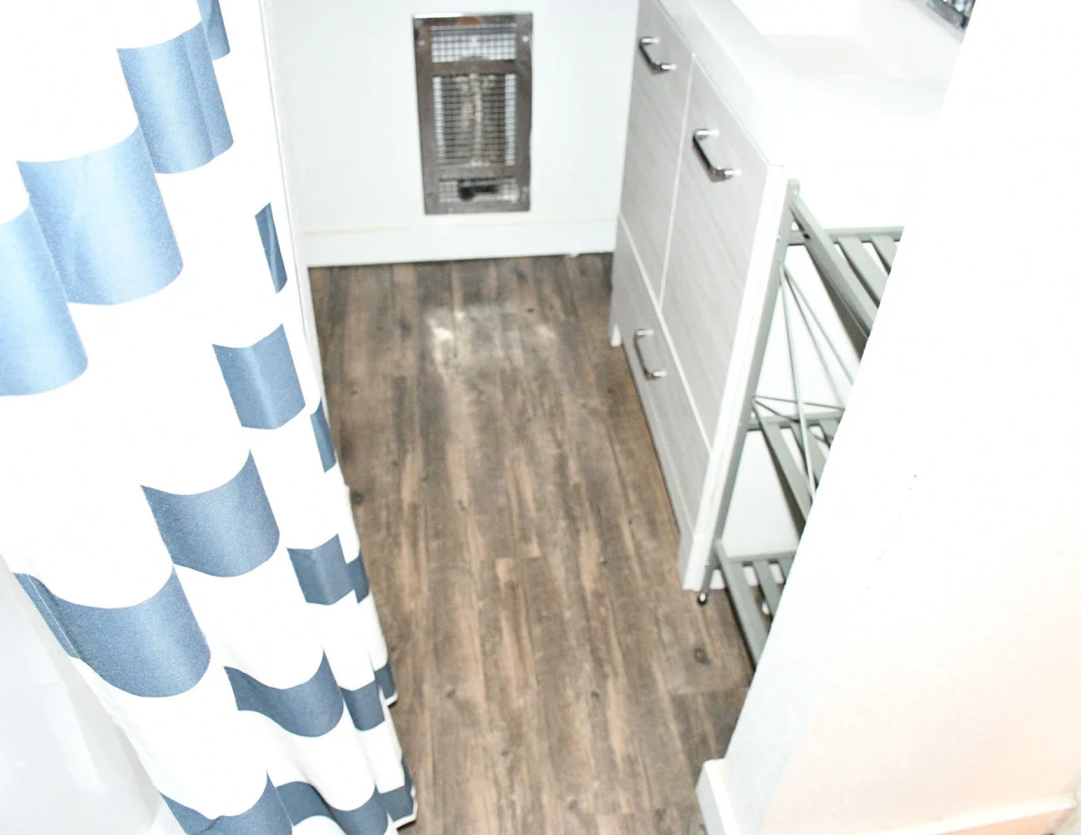 Bathroom floor beside striped shower curtain, vanity cabinet and wall heater.