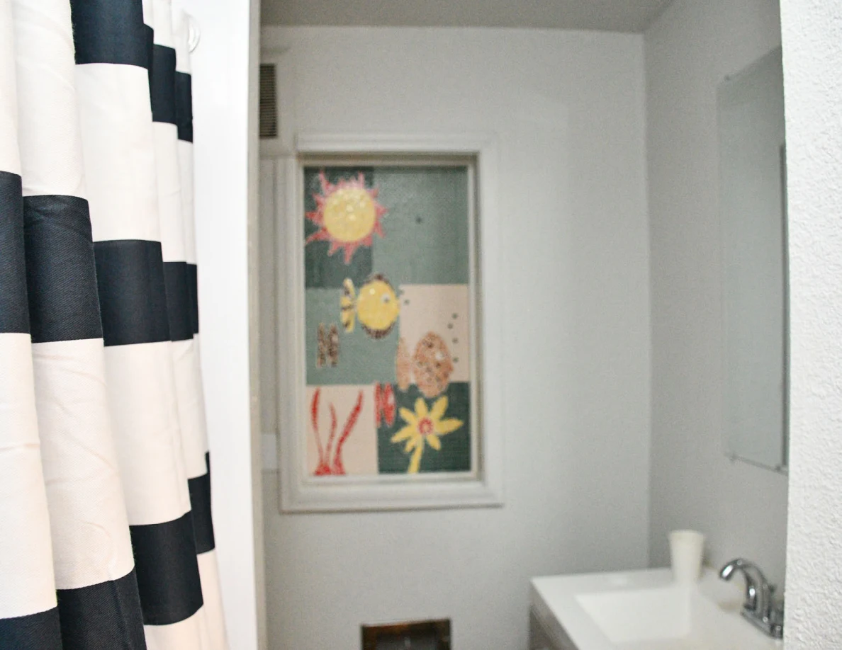 Bathroom window with colorful flower artwork, striped shower curtain and sink edge.