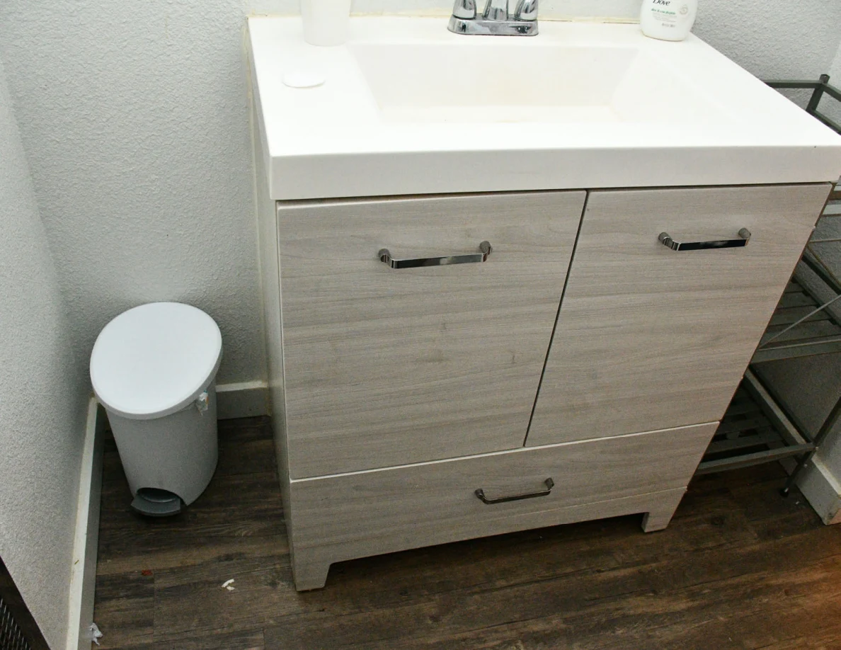 Bathroom sink vanity cabinet, small trash bin and shelving.