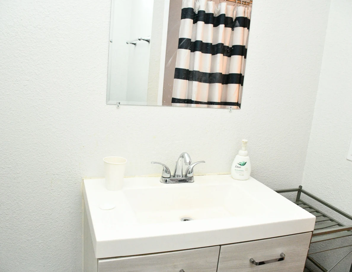 Bathroom sink, faucet, cabinet and wall mirror reflecting a striped curtain.