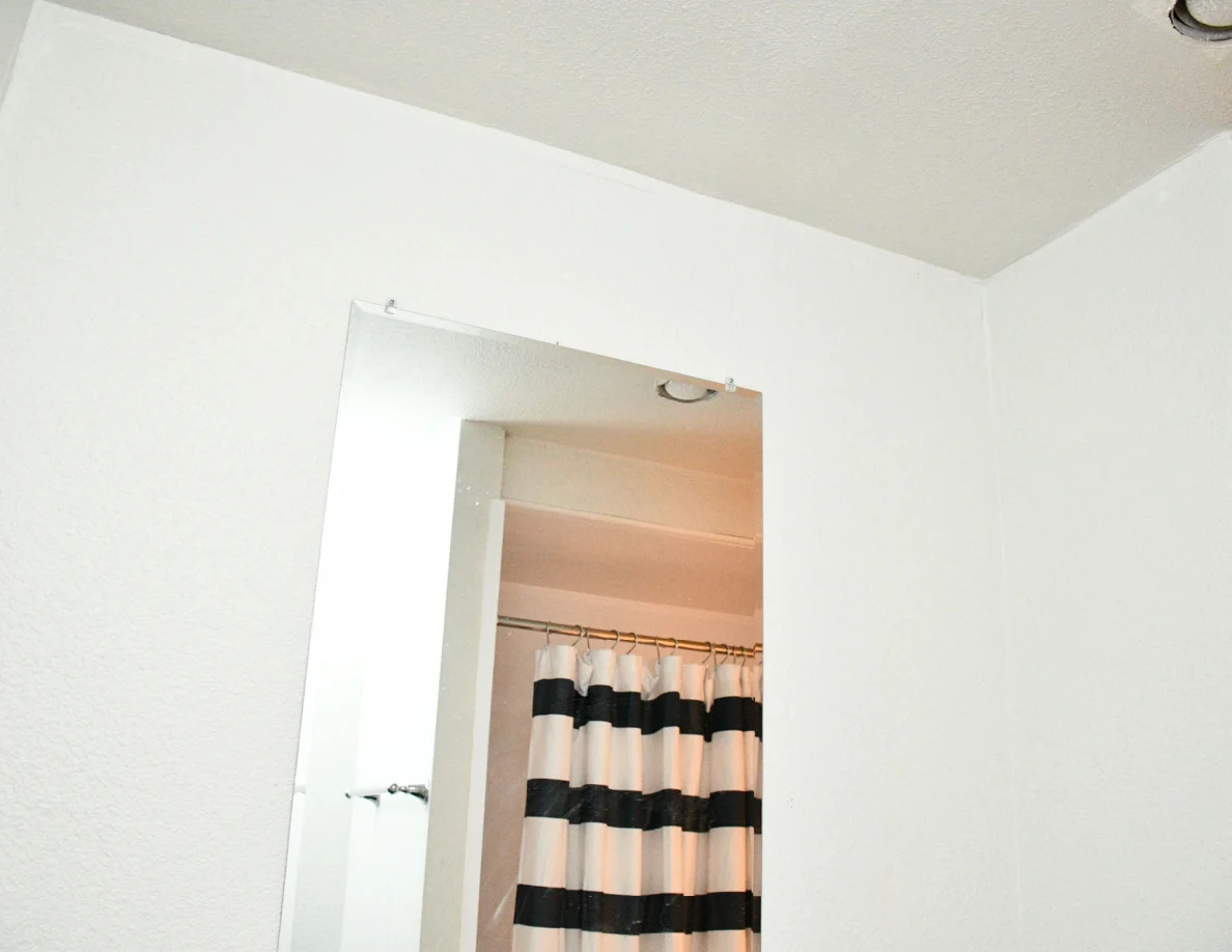 Upper bathroom wall and mirror reflecting a striped shower curtain.