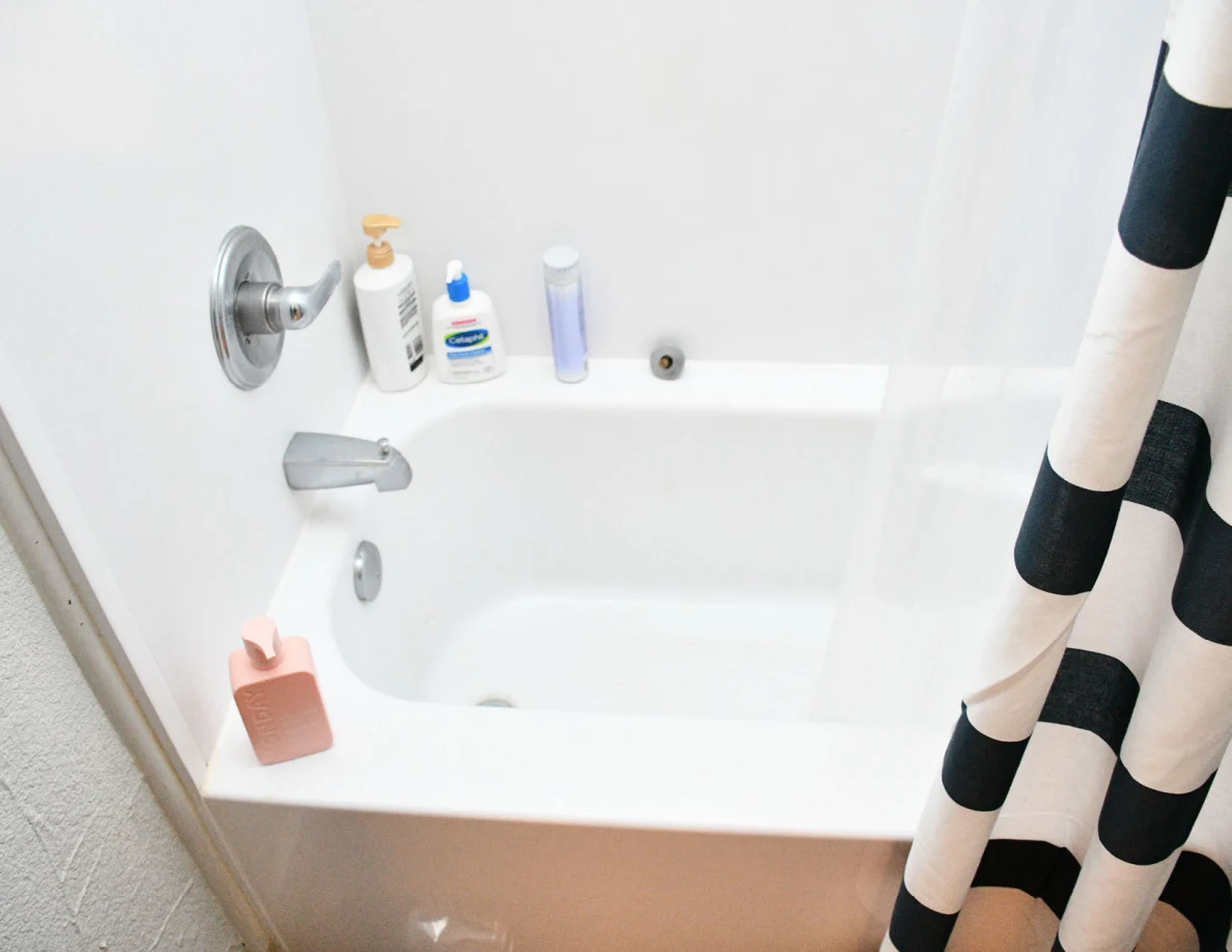 Bathtub with faucet, toiletries and striped shower curtain.