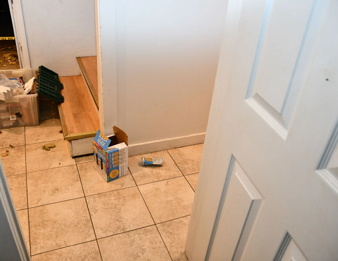 Tile entryway floor, open cardboard box and bottom of wooden stairs.