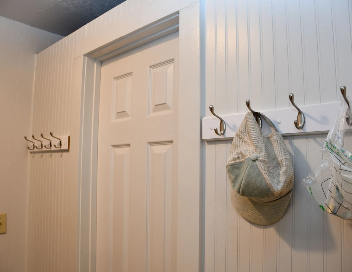 Closed interior door beside wall hooks holding caps.