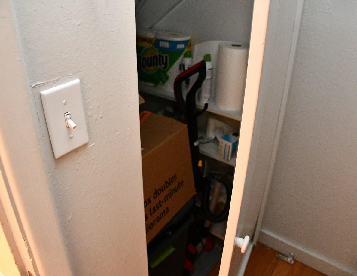 Open storage cupboard containing paper towels, cardboard boxes and cleaning equipment.