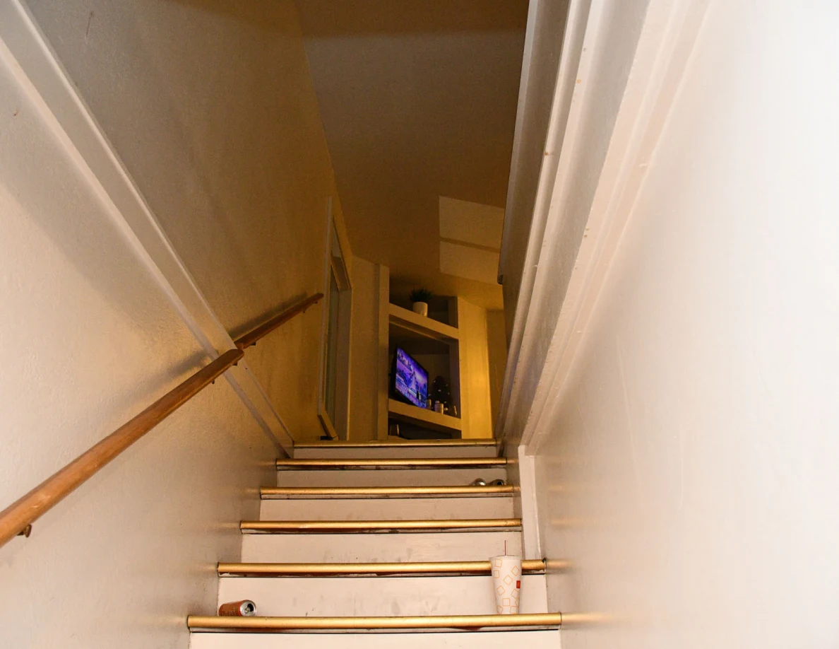 Upper staircase and handrail leading toward a television.