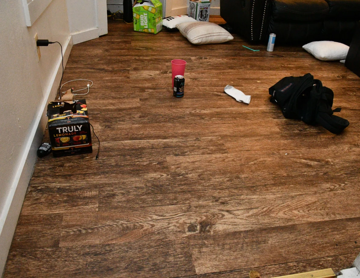 Wood-pattern room floor with cushions, a bag, cups and drink packaging.