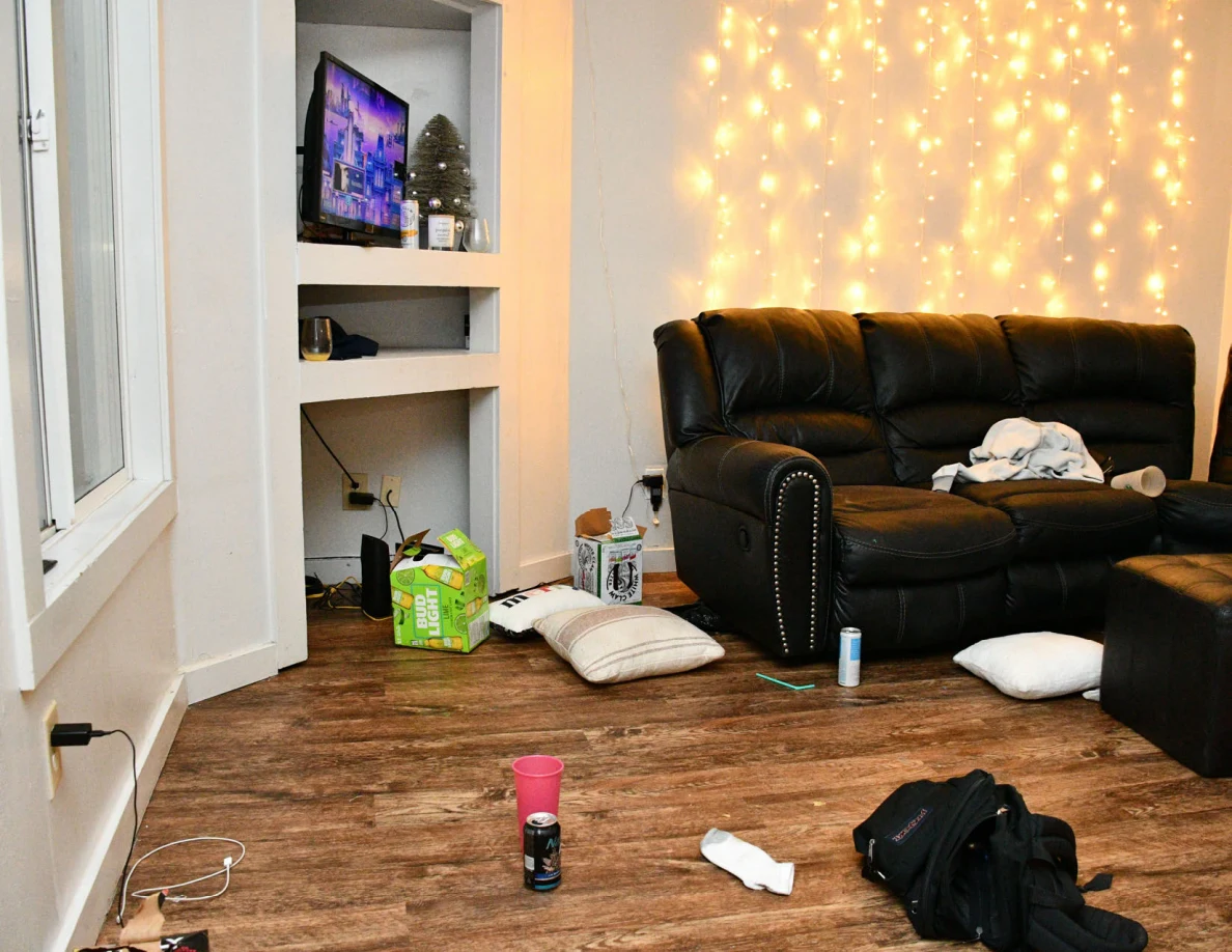 Living room with black sofa, television, string lights, cushions and objects on floor.