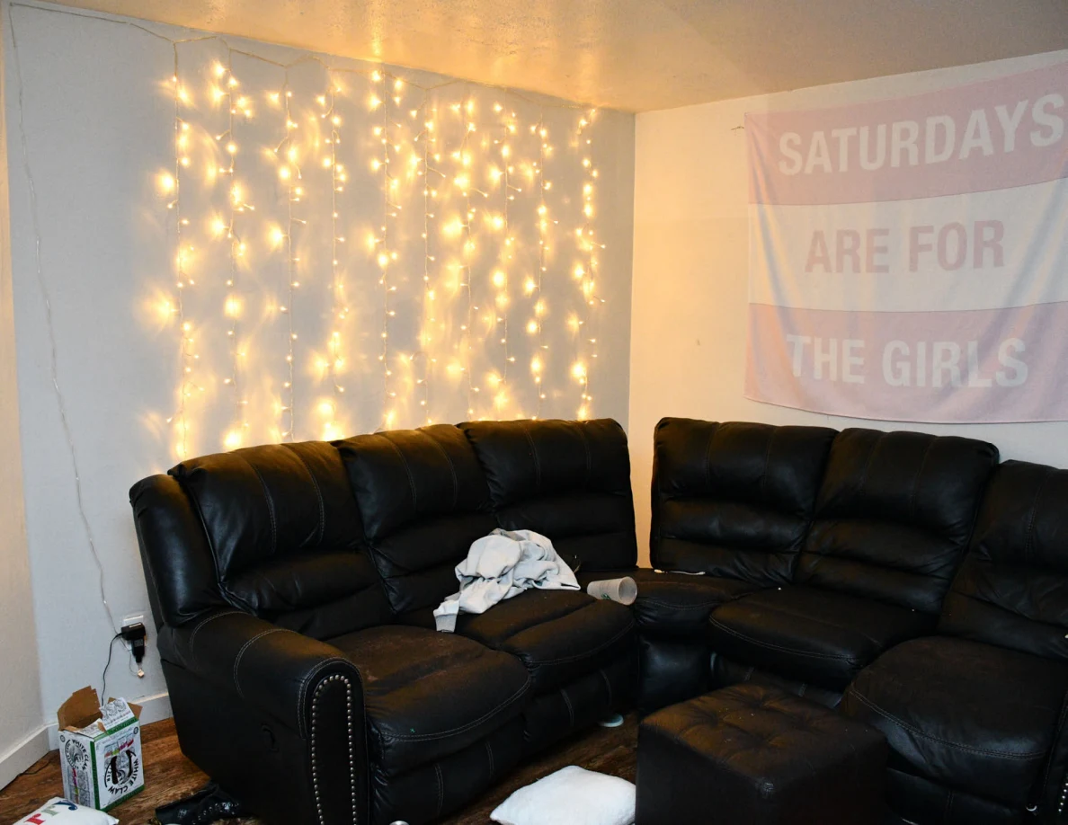 Black living-room sofas beneath string lights and a wall banner.