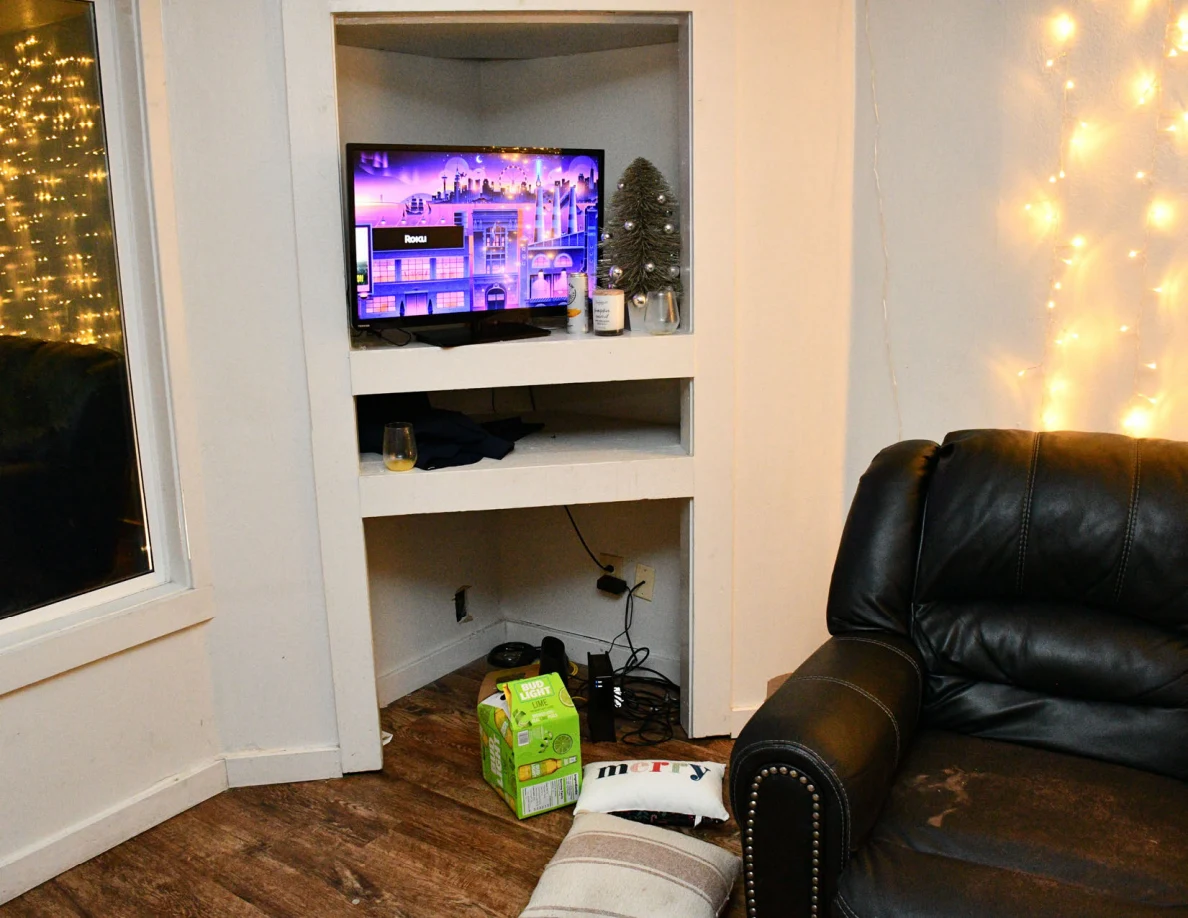Television on built-in shelves beside a black sofa, cushions and drink packaging.