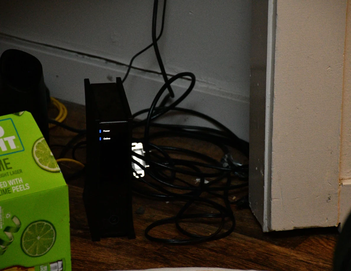 Black electronic device with indicator lights and coiled cables on the floor.
