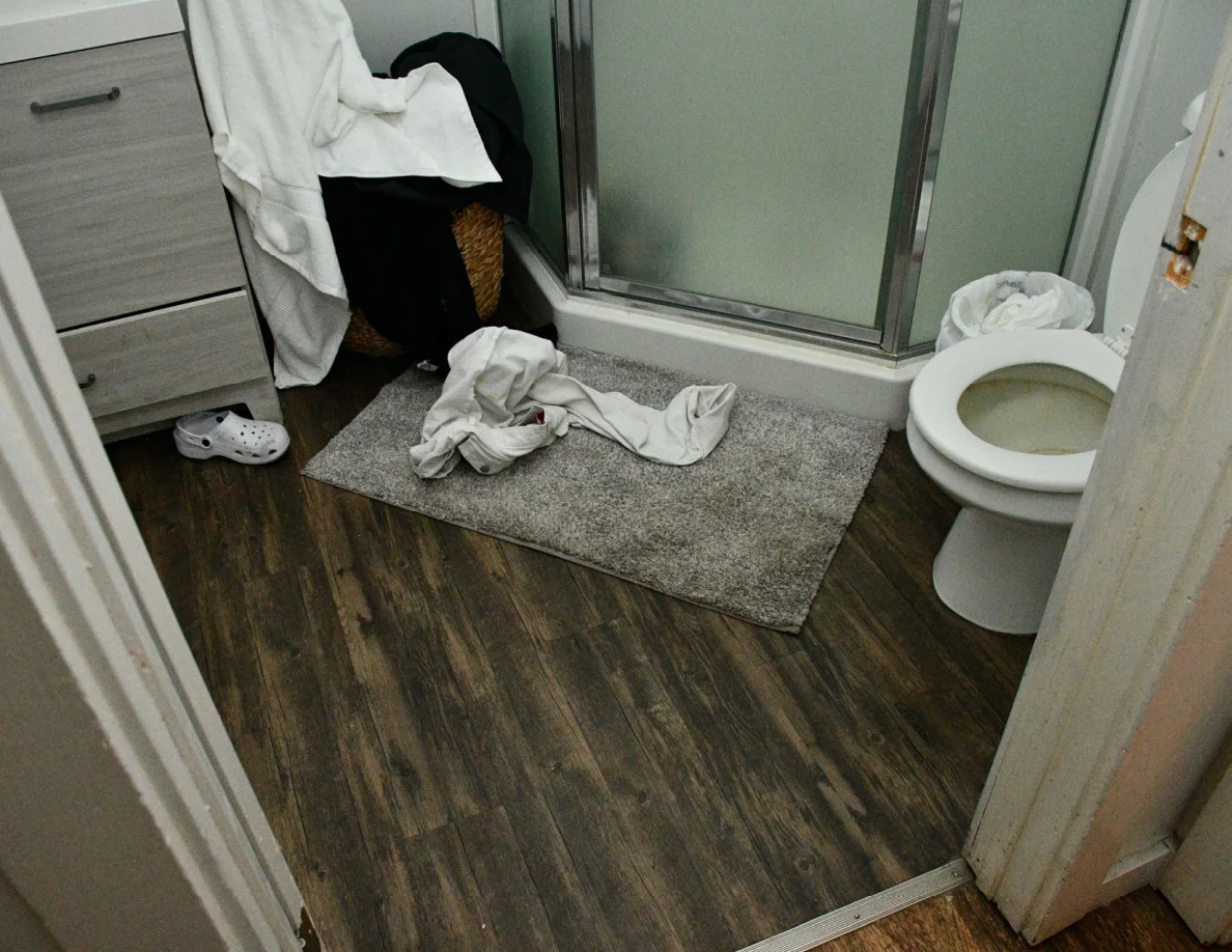 Bathroom with glass shower enclosure, toilet, vanity and towels on the floor.