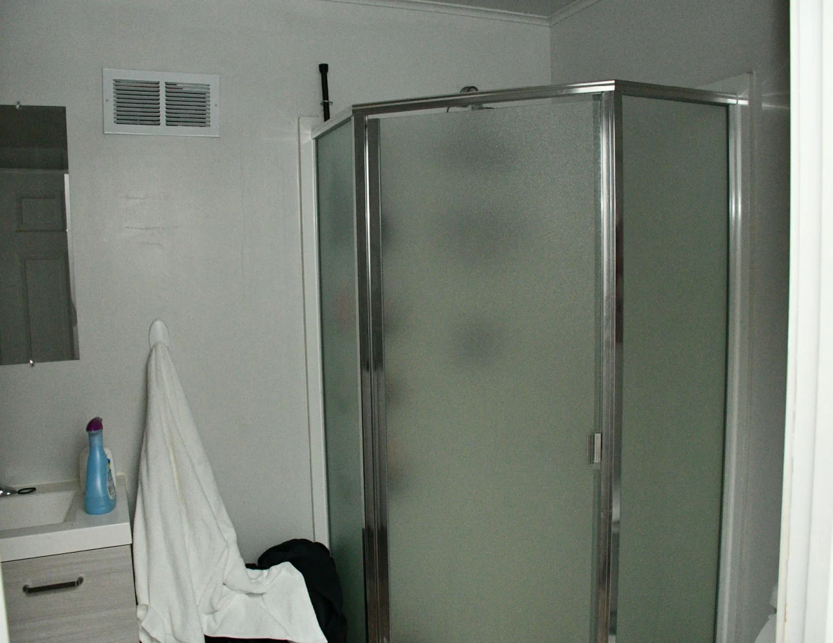 Glass shower enclosure beside hanging towels and a sink edge.