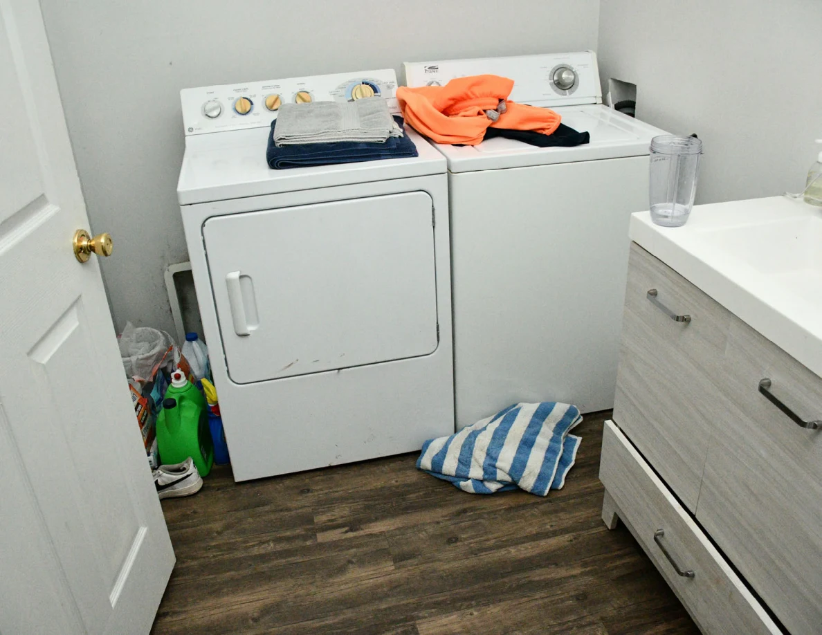 Bathroom laundry area with washing machine, dryer, vanity and striped towel on floor.