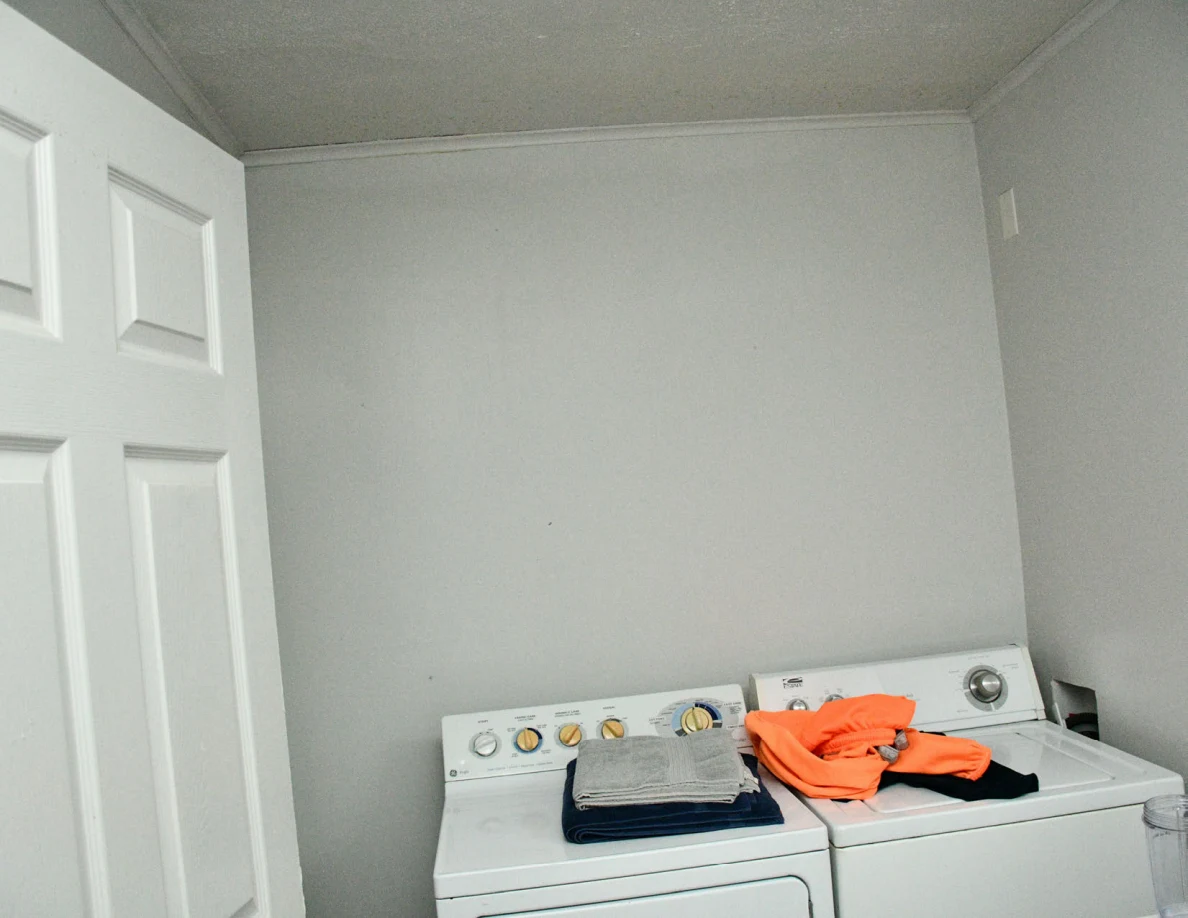 Washer and dryer with clothing on top beneath a plain wall.