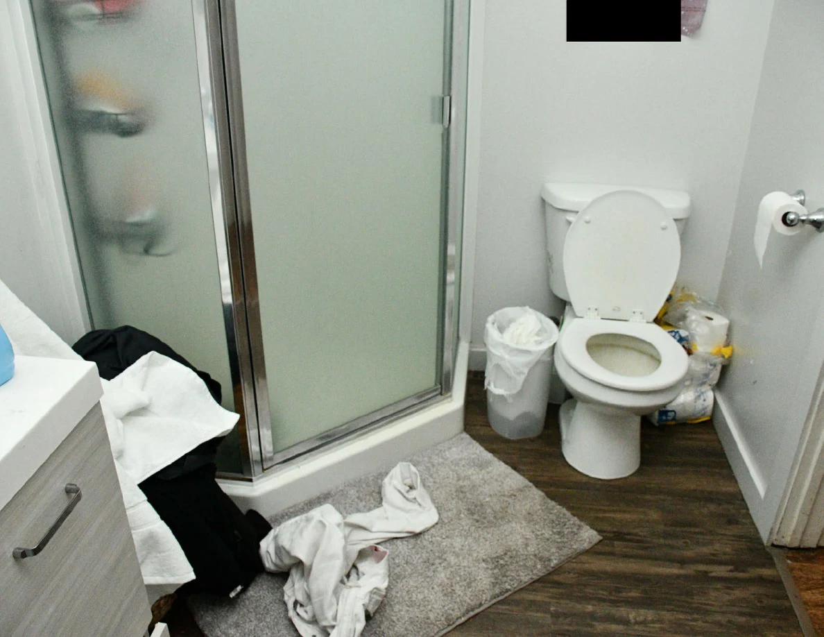 Bathroom toilet, glass shower enclosure, trash bins and towels on floor.