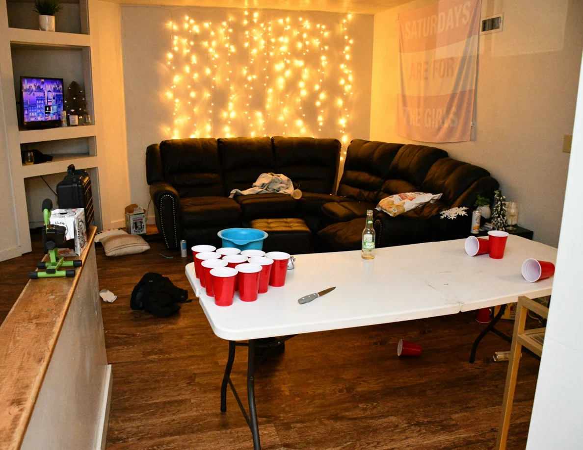 Living room with sofa, string lights and a white folding table holding a triangular arrangement of red cups.