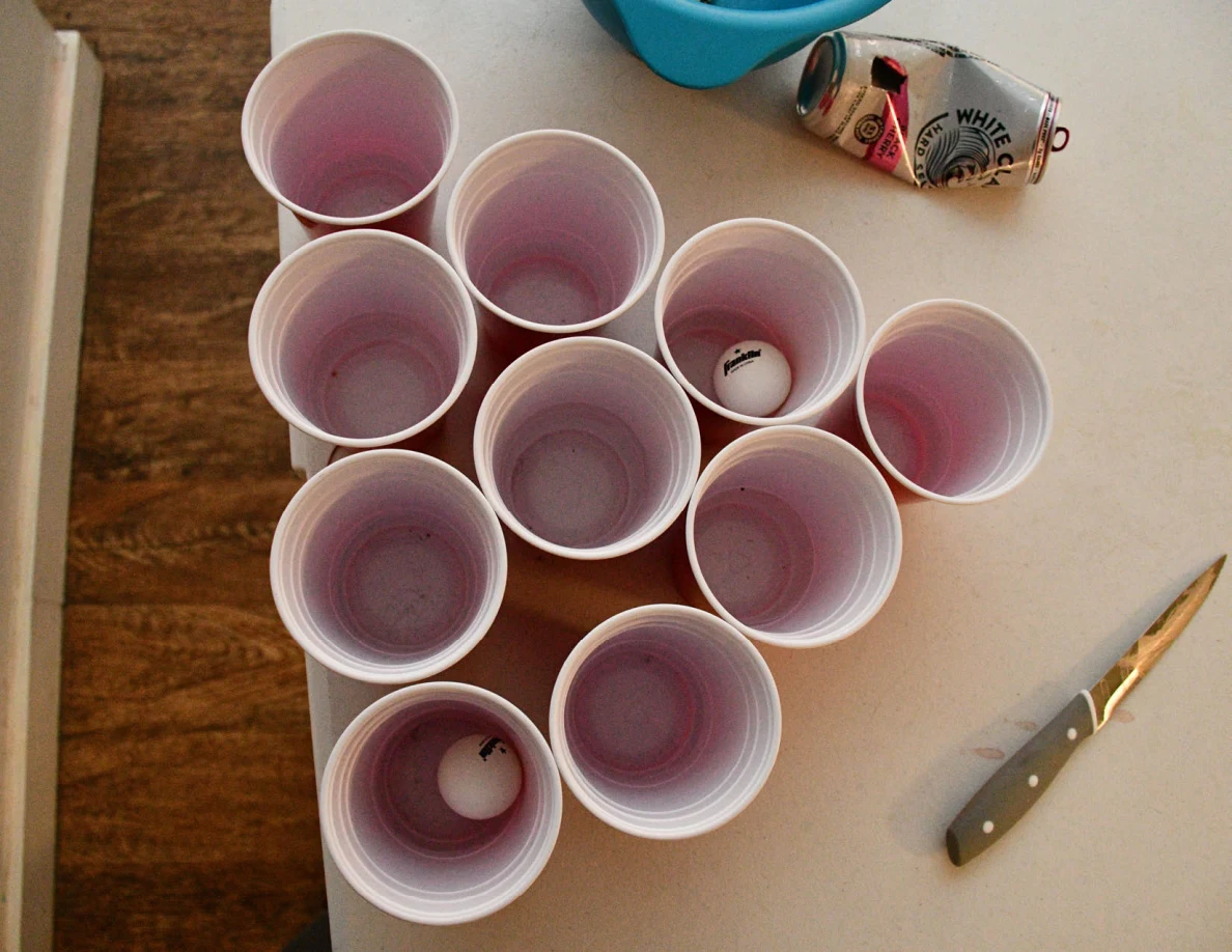 Overhead view of red cups in a triangular arrangement with a small white ball; knife beside the cups.