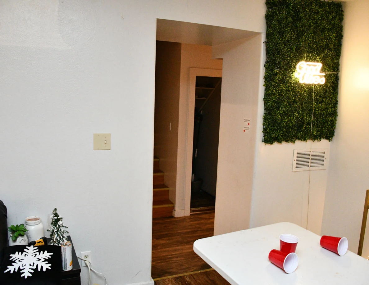 Room doorway beside decorative foliage panel and folding table with red cups.