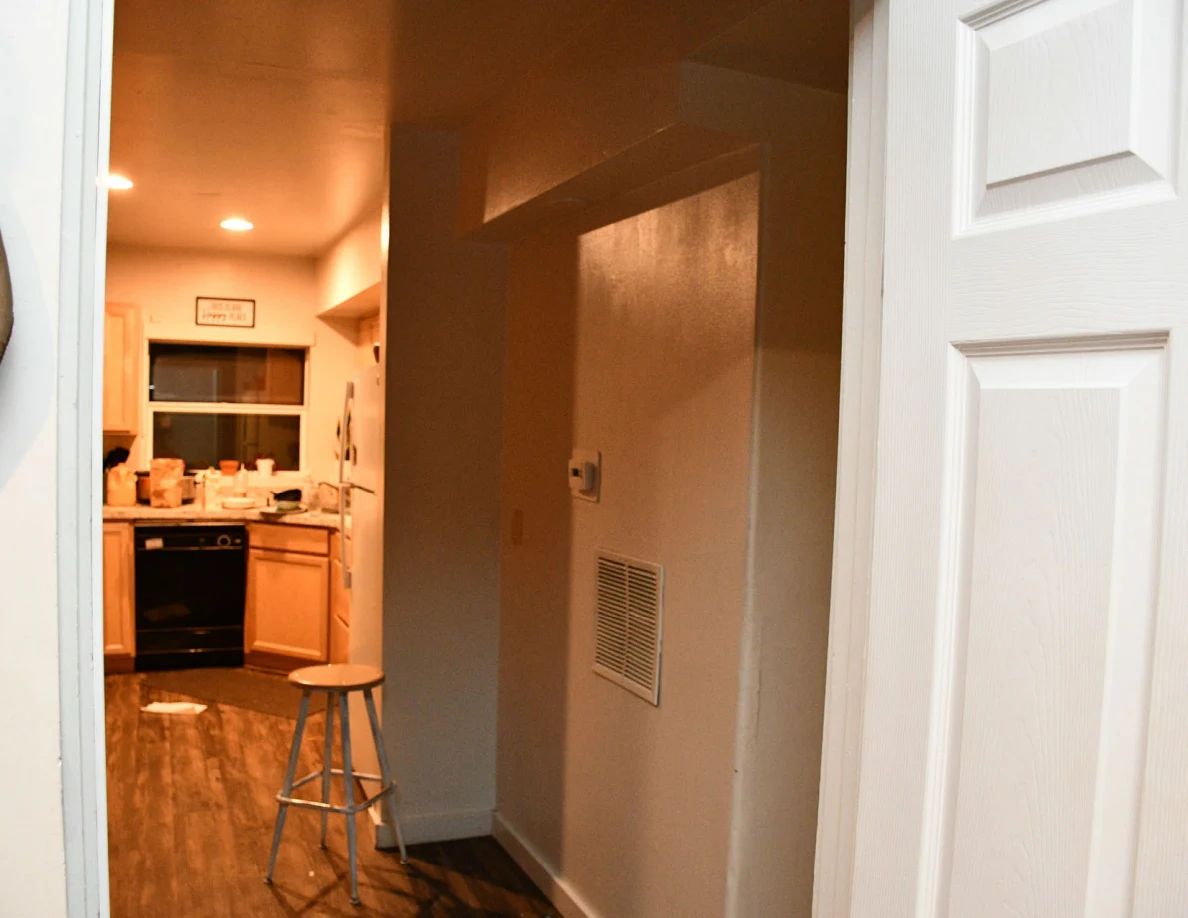 Hallway opening toward kitchen cabinets, dishwasher and stool.