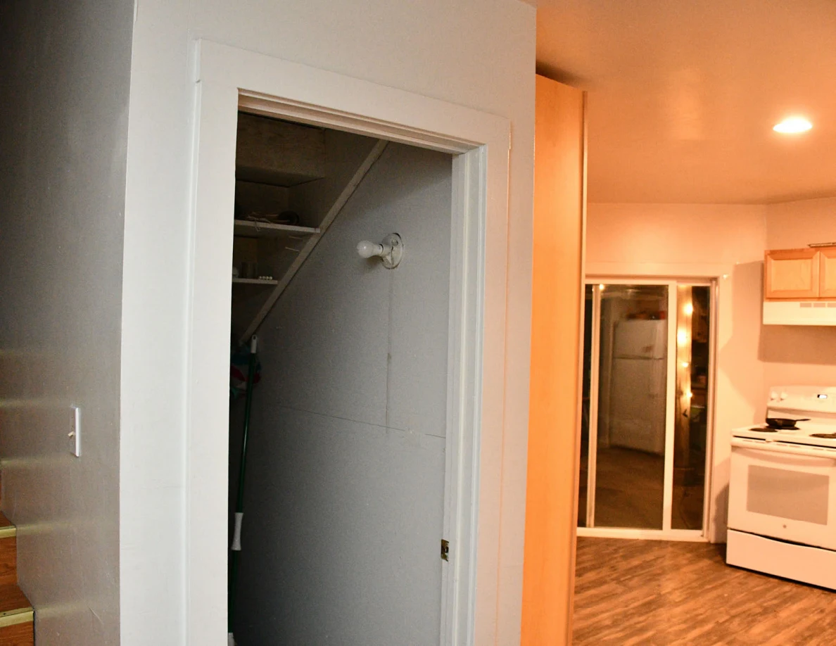 Open closet beside a kitchen with stove and sliding glass door.