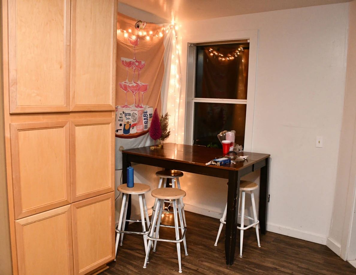 Tall wooden table and stools beside kitchen cabinets, window and string lights.