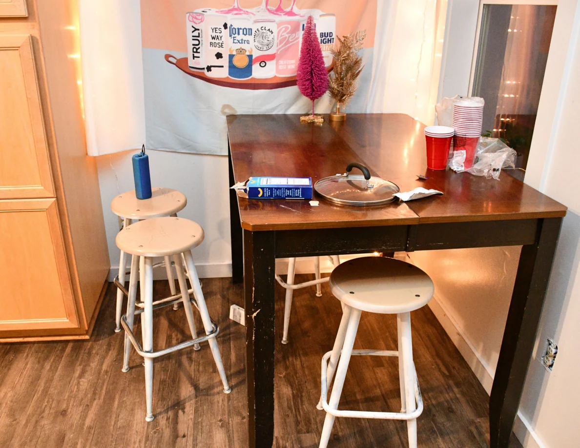 Wooden table and stools with cups, a pan lid and small tabletop decorations.