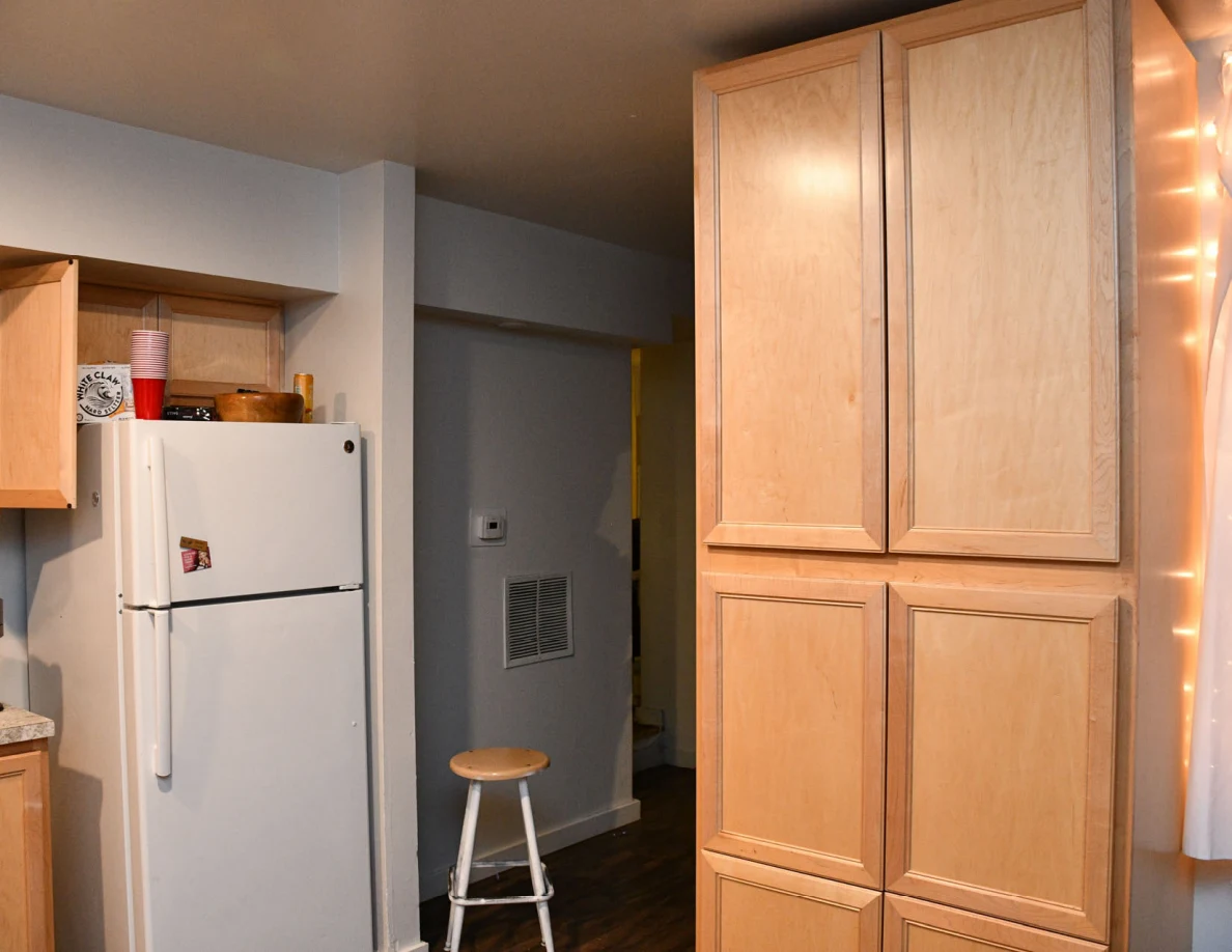 Tall kitchen cabinet beside refrigerator and hallway stool.