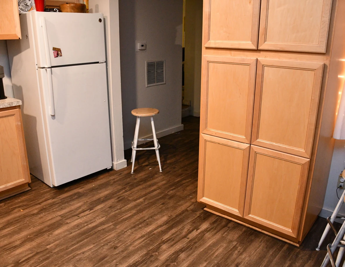 Kitchen refrigerator and tall cabinet with a stool in the hallway.