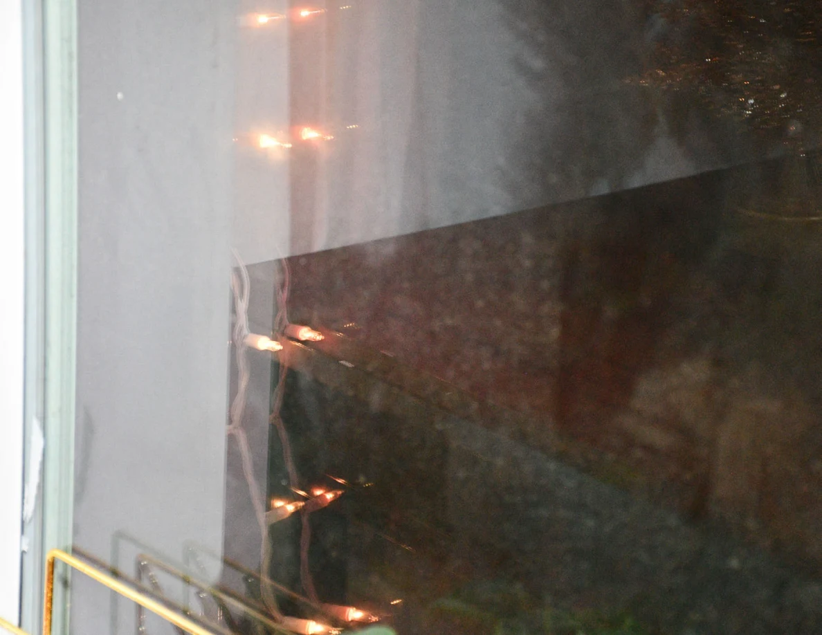 Close view of window glass reflecting a wooden table and string lights.