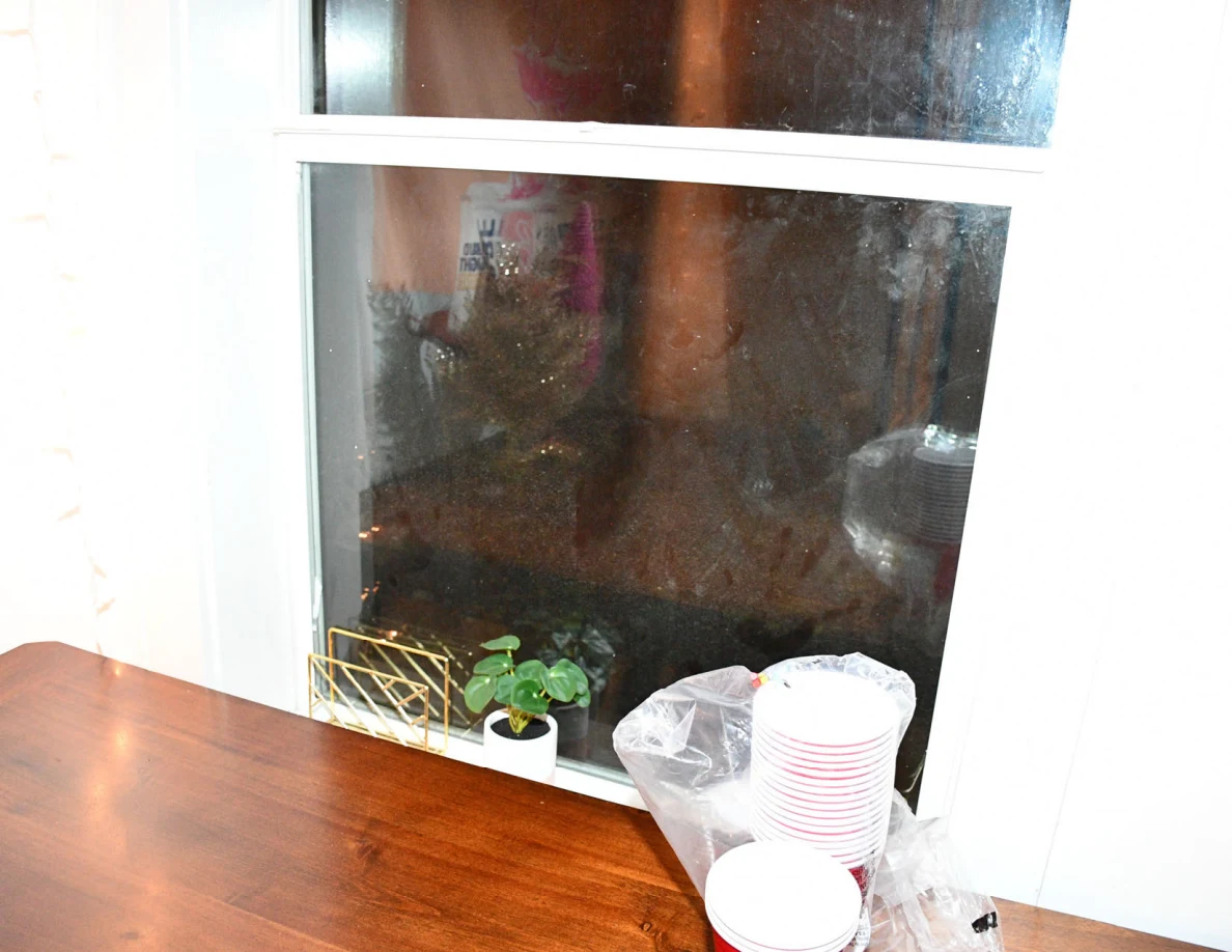 Window and sill above a wooden table with stacked cups and plastic packaging.
