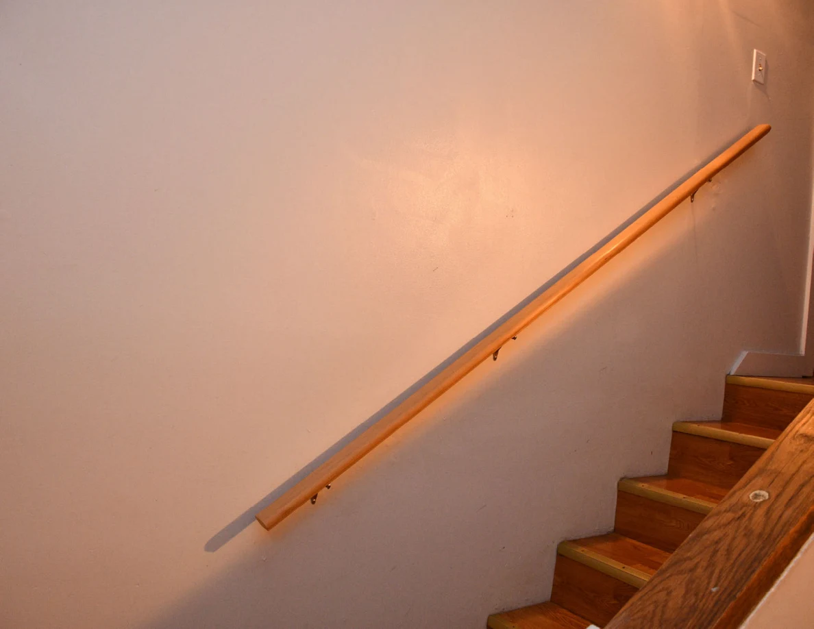 Wooden staircase and handrail against a plain wall.