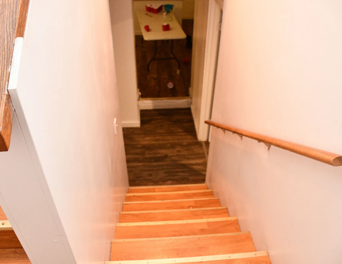 View down a wooden staircase toward a room with a cup-covered folding table.