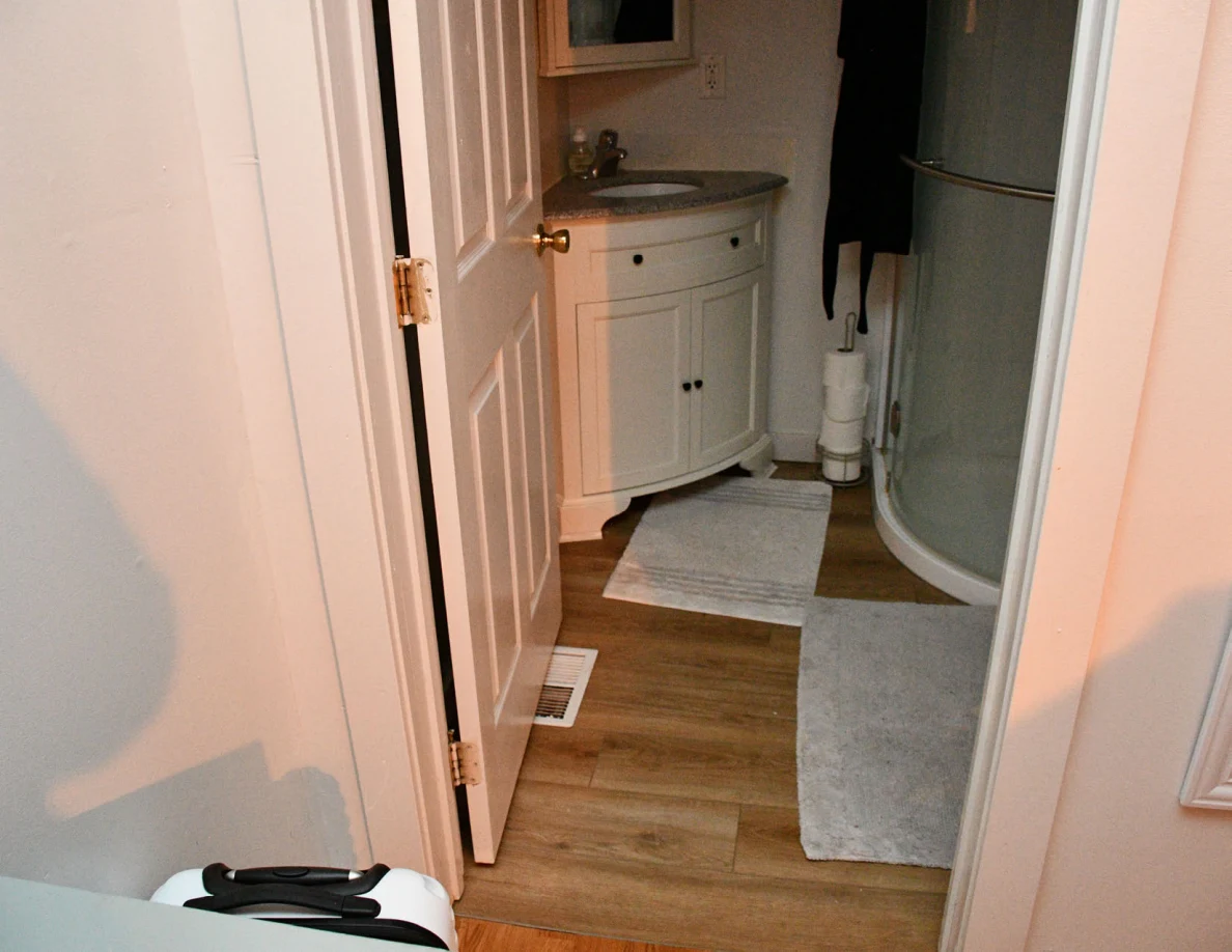 Bathroom doorway showing corner sink vanity, curved shower enclosure and rugs.