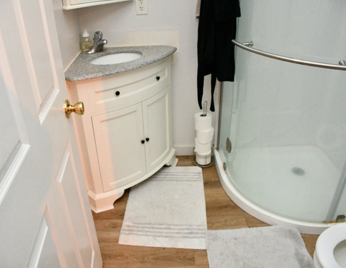 Corner sink vanity, bathroom rugs and curved shower enclosure.